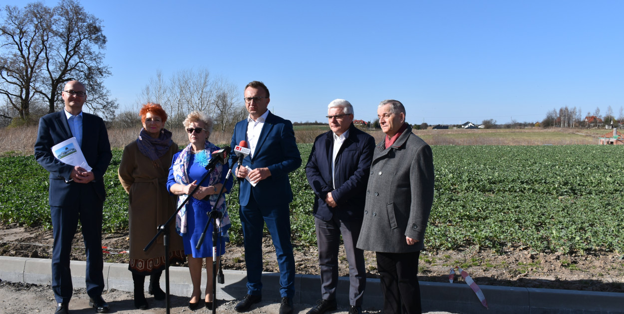 Konferencja prasowa na temat budowy zakładu. Za uczestnikami widać teren, na którym stanie placówka. 